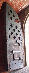 [Wooden door curved at top to match the arched opening of the fort. Door has wooden x patter with openings. A small hinged door is built into the bottom half.]